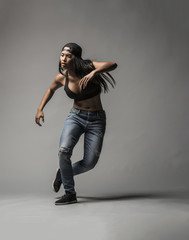 A beautiful black asian woman does an expressive contemporary urban dance move wearing jeans a sports bra and a black baseball cap