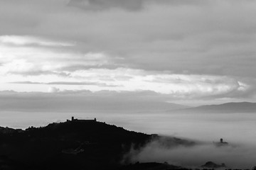 Beautiful view of Assisi town (Umbria) from behind, over a sea of fog at dawn