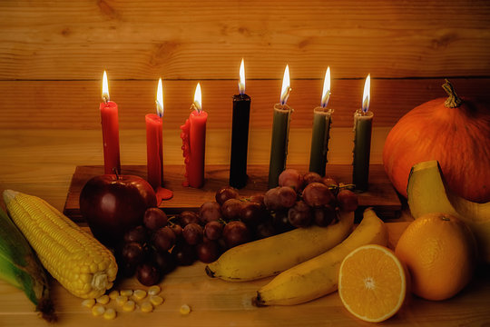 Kwanzaa holiday concept with decorate seven candles red, black and green, gift box, pumpkin,corn and fruit on wooden desk and background.