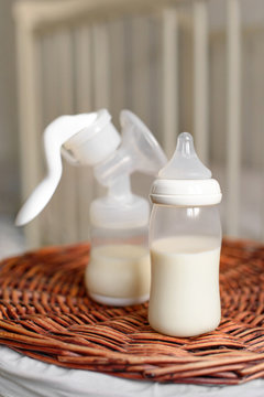 Breast pump and bottle with milk for baby on a straw basket. Kids room with a bed.