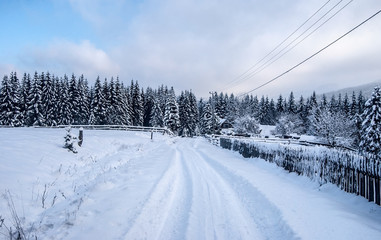 Fototapeta na wymiar winter countryside with snow covered road, isolated house with fence, forest and blue sky with clouds