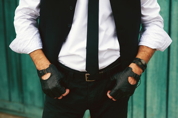 Stylish man wearing jeans , gloves and vest posing on a background of rough wooden wall , minimalist urban style clothing. Closeup