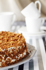 Homemade delicious honey cake with crumb. White tea set on background. Selective focus