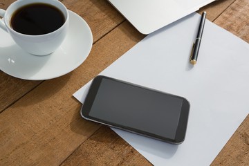 Laptop, mobile phone, black coffee, pen and paper on wooden