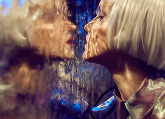 Close up futuristic neon lighted portrait of a girl with white bob hairstyle near wet glass