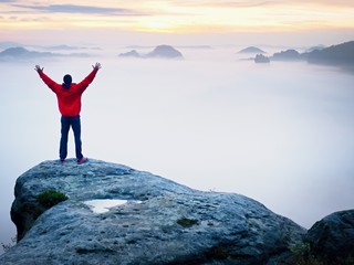 Tall tourist celebrate on the peak of the world . Orange thick fog bellow in deep valley. Dreamy daybreak