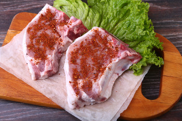 Raw pork steak with spices Leaves lettuce on wooden cutting board. Ready for cooking.