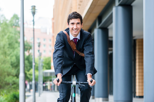 Active young man smiling while riding utility bicycle to his workplace in the morning in a modern European city