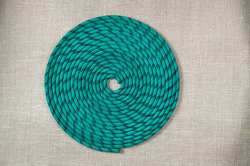 green rope for mountaineering or sailing in irregularly wound ring on textured fabric background