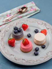 Small round berry cheesecakes on plate and blue background