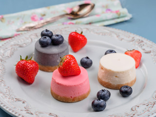 Small round berry cheesecakes on plate and blue background