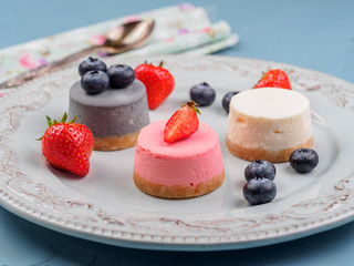 Small round berry cheesecakes on plate and blue background