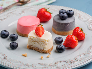 Small round berry cheesecakes on plate and blue background