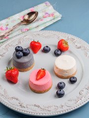 Small round berry cheesecakes on plate and blue background