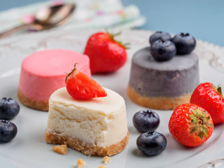 Small round berry cheesecakes on plate and blue background
