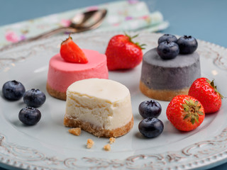 Small round berry cheesecakes on plate and blue background