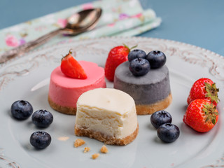 Small round berry cheesecakes on plate and blue background