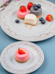 Small round berry cheesecakes on plate and blue background