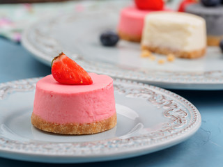 Small round berry cheesecakes on plate and blue background