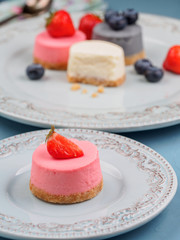 Small round berry cheesecakes on plate and blue background
