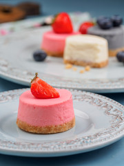 Small round berry cheesecakes on plate and blue background