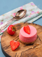 Small round strawberry cheesecakes on wooden desk and blue background