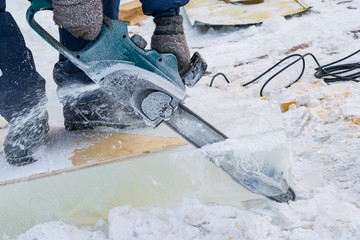 A worker saws a saw chunks of ice for building ice sculptures, winter landscape. Preparation of the New year and the decoration of the streets