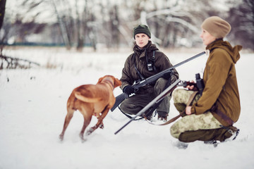 two hunters with rifles in a snowy winter forest.