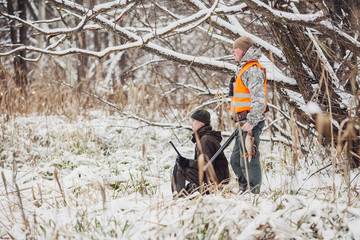 Male hunters armed with a rifle, standing in a snowy winter forest with duck prey