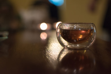 Transparent small glass of Chinese black tea on a table, shot contre-jour to candlelight