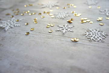 White paper snowflakes and gold sequins on light wooden background with copy space for greetings, christmas and new year, minimalistic design