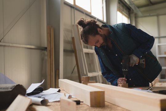 Carpenter making hole in wooden block with screw gun