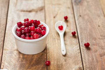 A small bowl of cranberries on a wooden table with  a white spoon © ozhukovaphoto