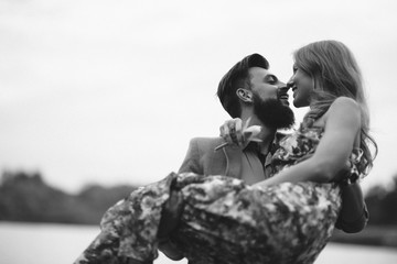 A bearded hipster guy carries a beloved girl in her arms and asks for hands and a heart.