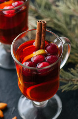 Mulled wine. Christmas hot drink with citrus, apple and spices in a glass cup on a black background.