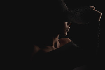 Dramatic dark studio portrait of elegant and luxury woman in black wide hat and black dress. Hidden eyes.