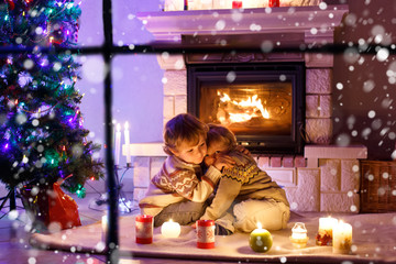 Fototapeta na wymiar Cute toddler boys, blond twins playing together and lookinig on fire in chimney. Family celebrating xmas holiday