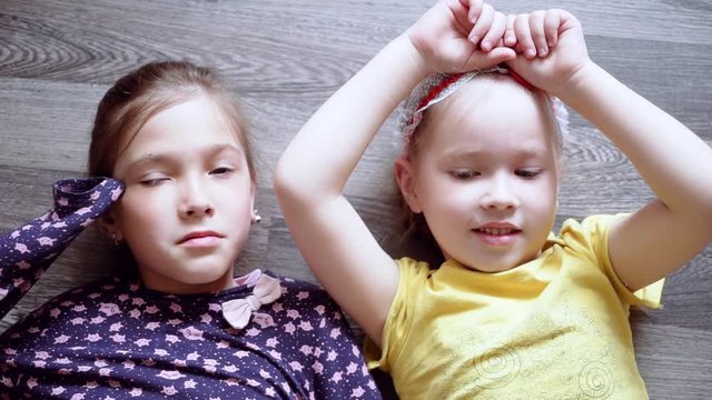 little girls lie on the floor and look at the camera. two sisters.