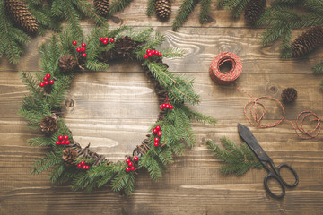 Christmas wreath made of spruce branches with holly berries on wooden board. Wreath workshop. Top...