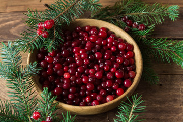 Red berries in a wooden plate on a wooden background with spruce branches. Cranberry. © ozhukovaphoto