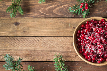 Red berries in a wooden plate on a wooden background with spruce branches. Cranberry. - 183929657