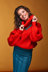 Colorful portrait of amazing smiling brunette woman wearing orange red sweater and turquoise skirt in studio with orange background