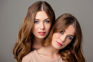 portrait of beautiful twin sisters with bright makeup looking at camera isolated on grey