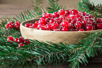 Red berries in a wooden plate on a wooden background with spruce branches. Cranberry. - 183929868