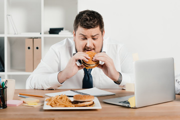 overweight businessman eating junk food in office