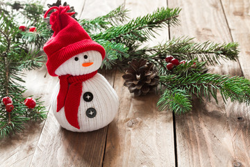 White fabric snowman in a red hat on a wooden background with spruce branches. Christmas background. - 183931062