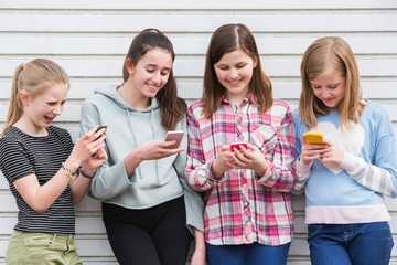 Group Of Young Girls Outdoors Looking At Messages On Mobile Phones
