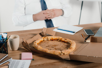cropped view of fat businessman eating pizza at workplace