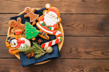 Plate with homemade glazed different shapes of christmas cookies. Top view and wooden backdrop.