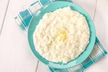 Rice milk porridge with nuts and raisins in a blue dish on a white wooden table.